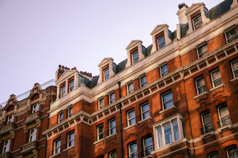 The image shows the facade of a historic townhouse with a white ornate archway framing a black main door, located on a street in Mayfair. The building features red brickwork with contrasting white sto