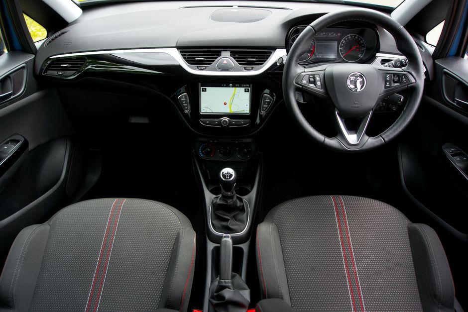 The interior of a compact car showing the dashboard, steering wheel, and front seats. The dashboard features a central touchscreen display with a GPS navigation map, flanked by air vents and control b